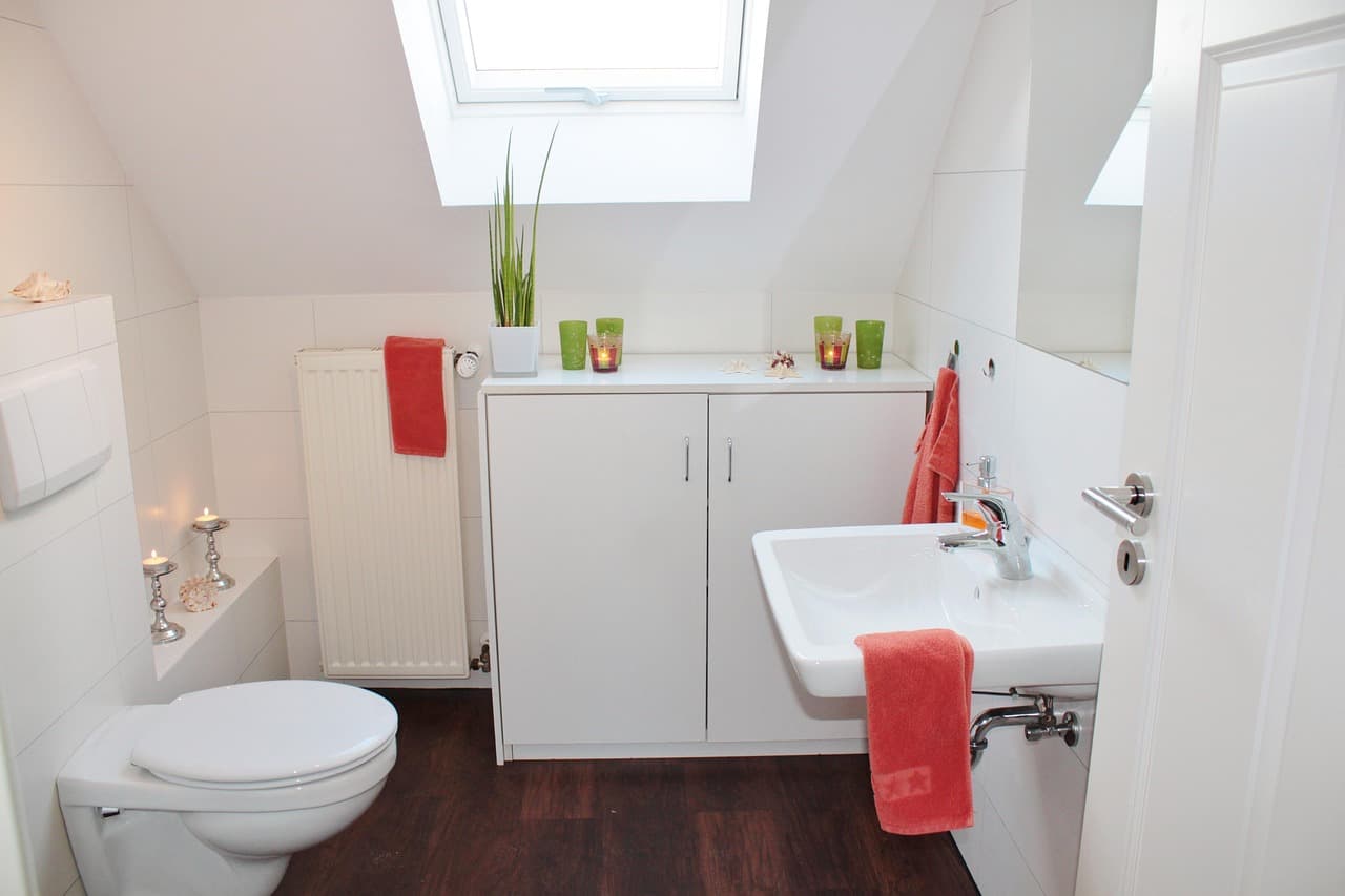 A small white bathroom with a skylight and red towels