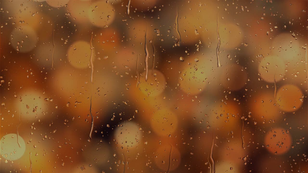 Rain on a window at night, street lamps blurred behind it