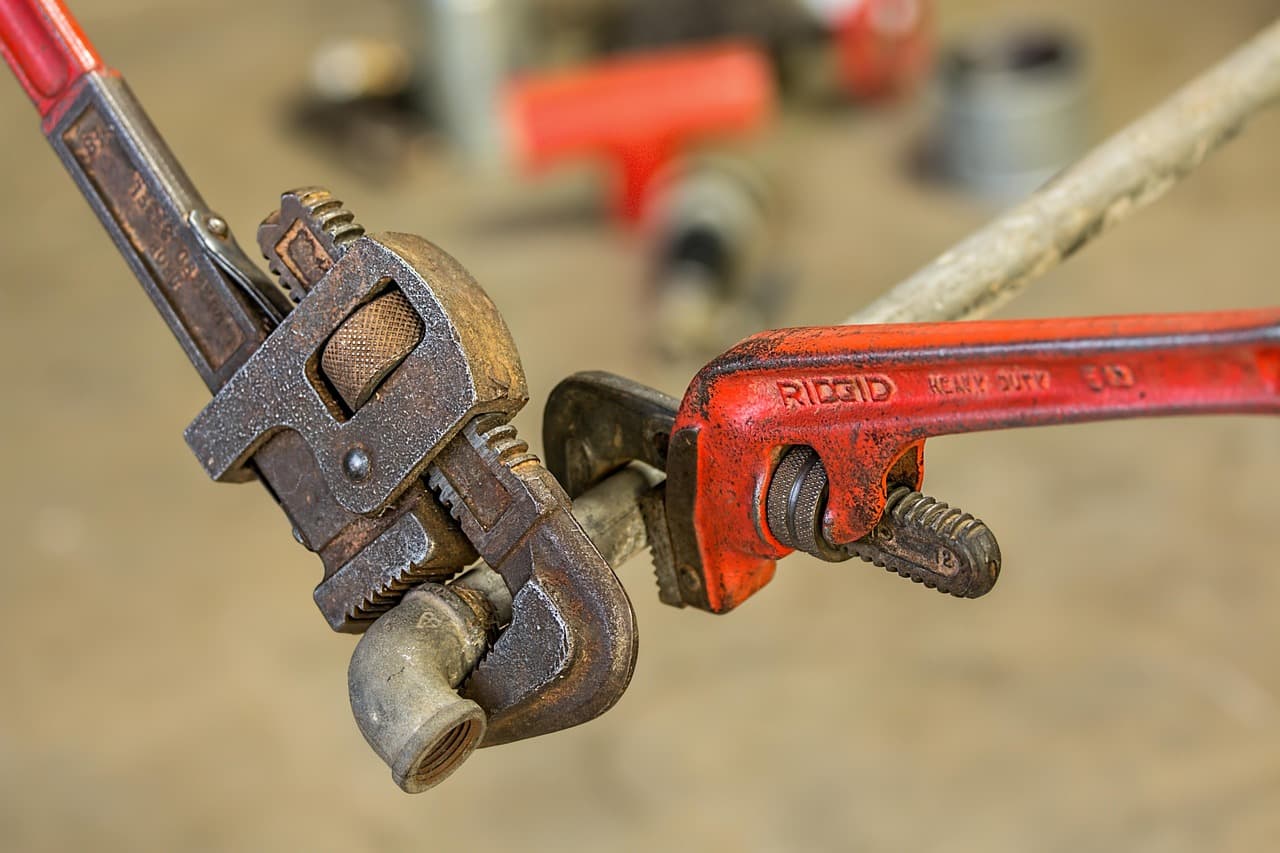Two pipe wrenches, one red, gripping a pipe